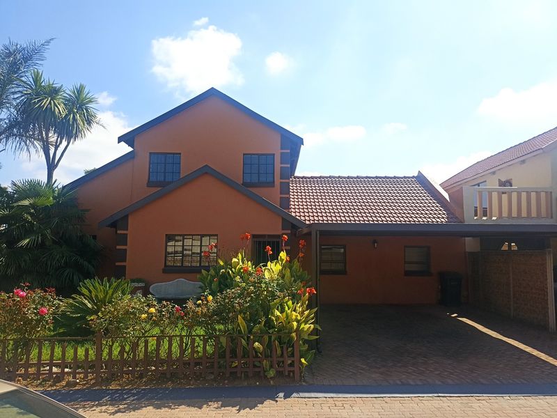 Front elevation of a two-story house featuring a paved driveway, integrated carport, and established garden with a timber fence.