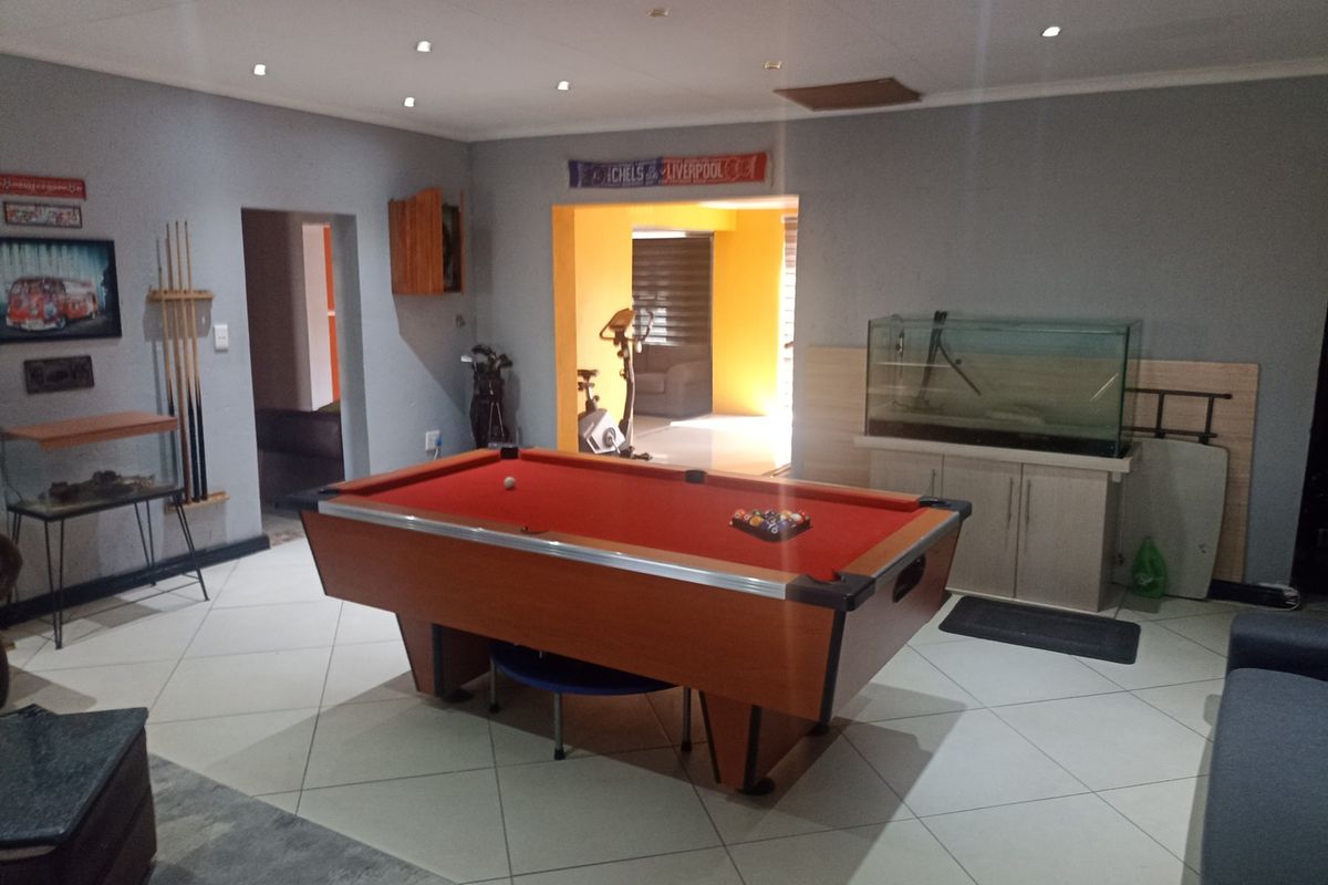 Spacious living area currently utilized as a games room, featuring tiled flooring and recessed lighting, with an open transition to adjacent living spaces.