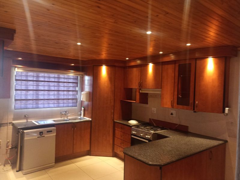 A functional kitchen featuring warm wooden cabinetry, granite countertops, a gas hob, and a distinctive wooden tongue and groove ceiling with recessed lighting.