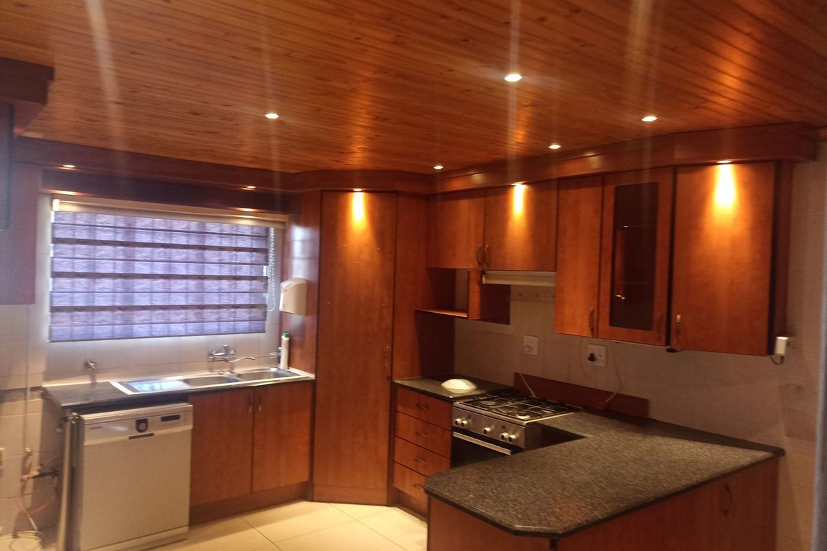A functional kitchen featuring warm wooden cabinetry, granite countertops, a gas hob, and a distinctive wooden tongue and groove ceiling with recessed lighting.