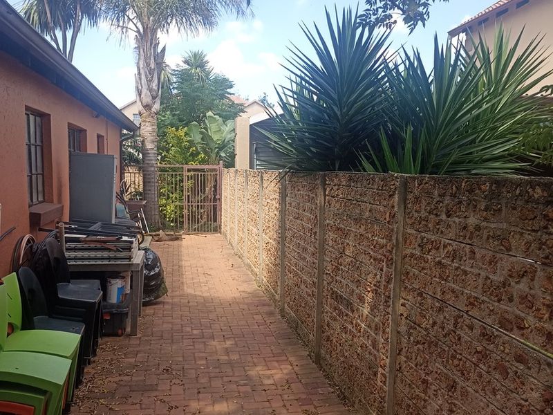 A side walkway featuring brick paving and a precast concrete boundary wall, leading towards a metal gate in the rear garden area.