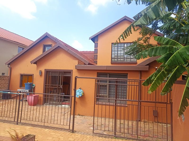 Rear view of the house featuring a paved patio area, security gates, and tiled roofing with orange exterior walls.