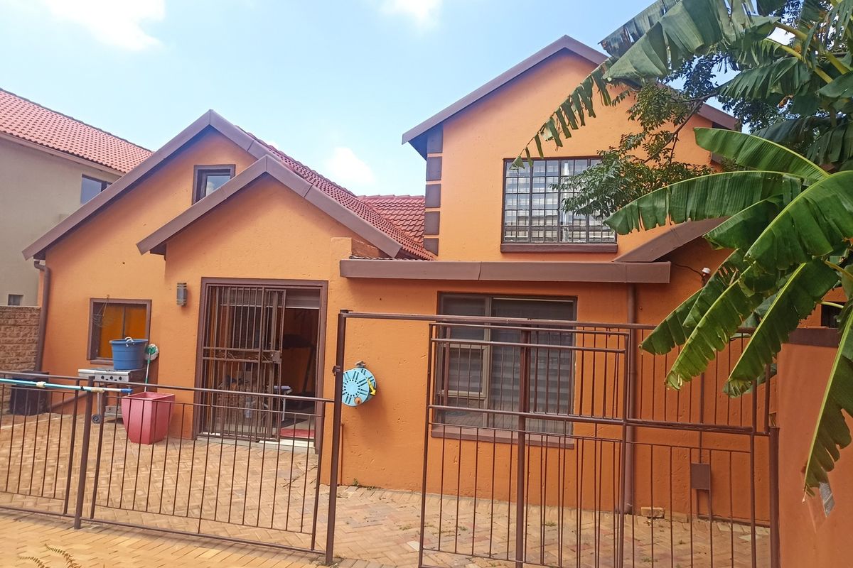 Rear view of the house featuring a paved patio area, security gates, and tiled roofing with orange exterior walls.