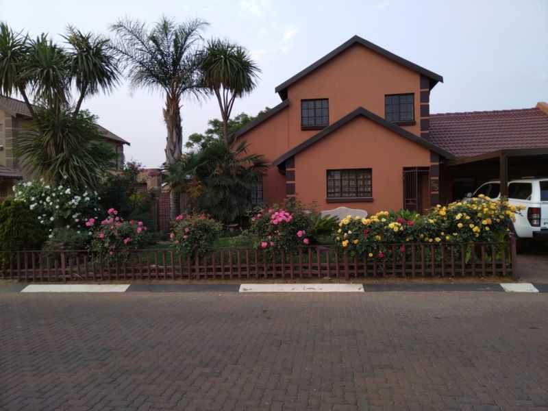 Front elevation of a two-story residential house featuring a paved driveway, carport, and established garden with security features.