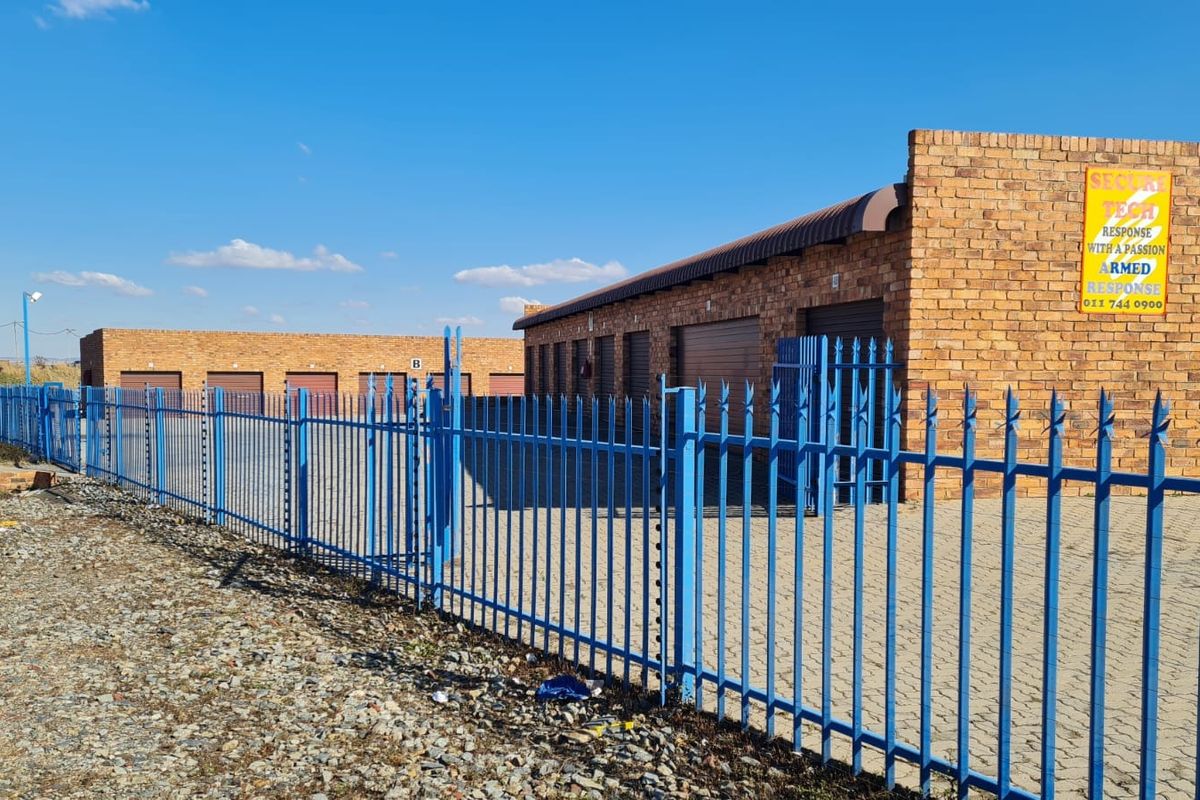 Industrial storage facility featuring face brick construction, multiple roller shutter doors, and secure perimeter palisade fencing with integrated electric security.