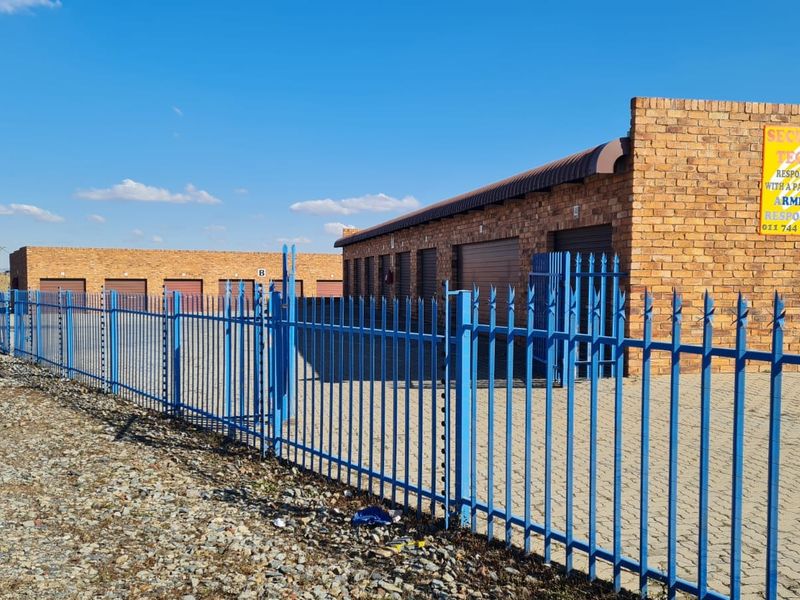 Industrial storage facility featuring face brick construction, multiple roller shutter doors, and secure perimeter palisade fencing with integrated electric security.