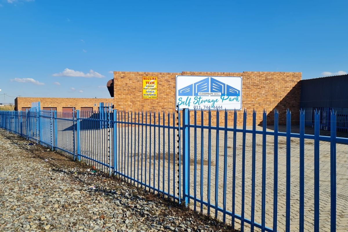 Front exterior view of the industrial self-storage facility featuring brick construction, secure steel palisade fencing, and paved driveway access.