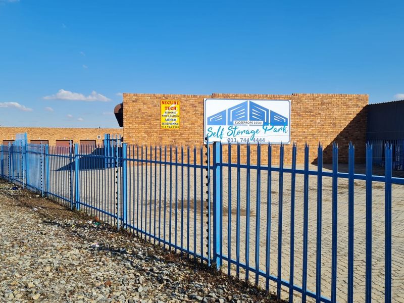 Front exterior view of the industrial self-storage facility featuring brick construction, secure steel palisade fencing, and paved driveway access.