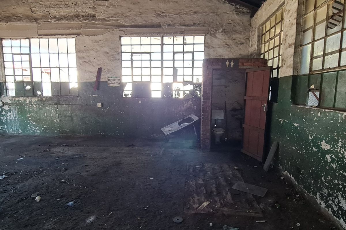 Spacious industrial utility area featuring exposed brickwork, steel-framed windows, concrete flooring, and an integrated toilet cubicle, requiring significant renovation and refurbishment.