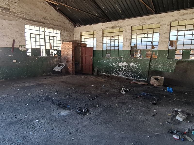 A large, vacant industrial utility space featuring exposed brick walls, high pitched ceilings, and multiple steel-framed windows requiring significant maintenance and refurbishment.