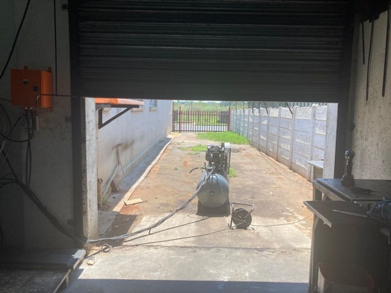 Industrial garage space featuring a large roller shutter door opening onto a concrete driveway and enclosed by a precast boundary wall.