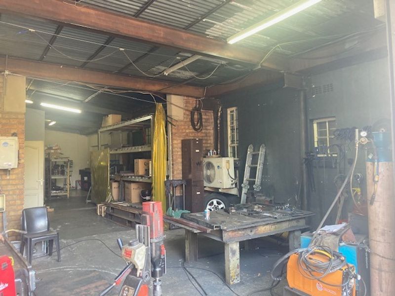 Industrial utility space featuring exposed steel beams, brick walls, and corrugated metal ceiling, currently utilized as a workshop area.