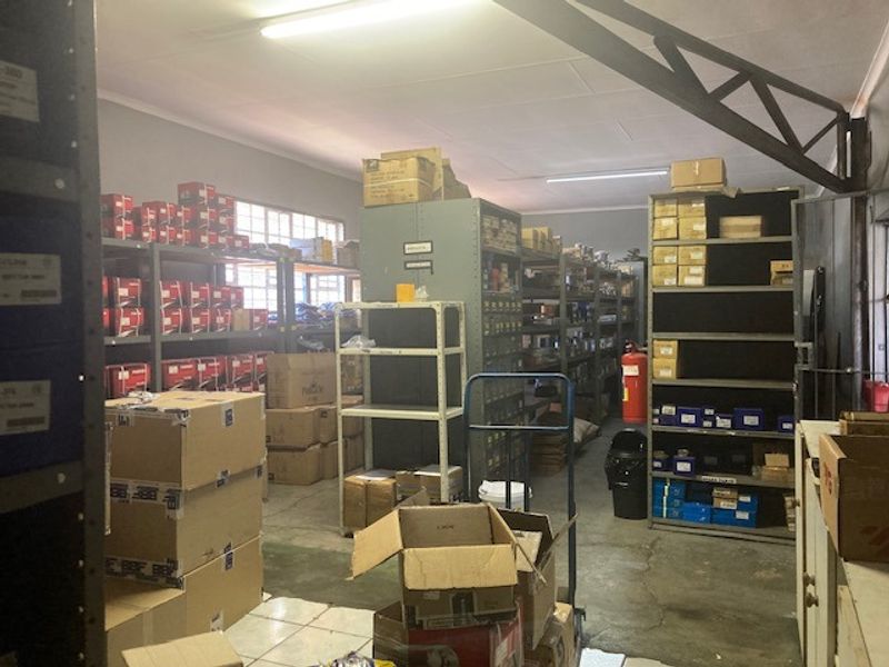 Industrial utility or storage space featuring concrete flooring, fixed steel shelving units, and overhead fluorescent lighting, suitable for warehouse or inventory management purposes.