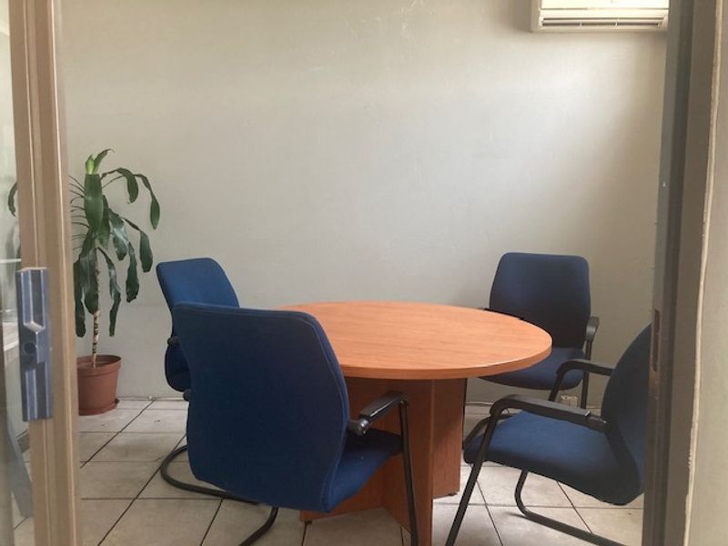 A functional office space featuring tiled flooring and a wall-mounted air conditioning unit, suitable for a meeting or workspace area.