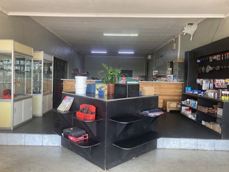 Industrial retail or workshop space featuring built-in display cabinets, fixed shelving units, and a raised platform area with fluorescent lighting.
