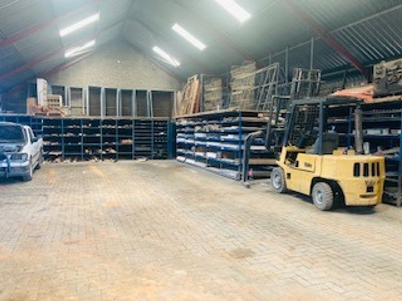 Spacious industrial warehouse or utility space featuring high pitched ceilings, skylights, durable paved flooring, and extensive built-in metal storage shelving.