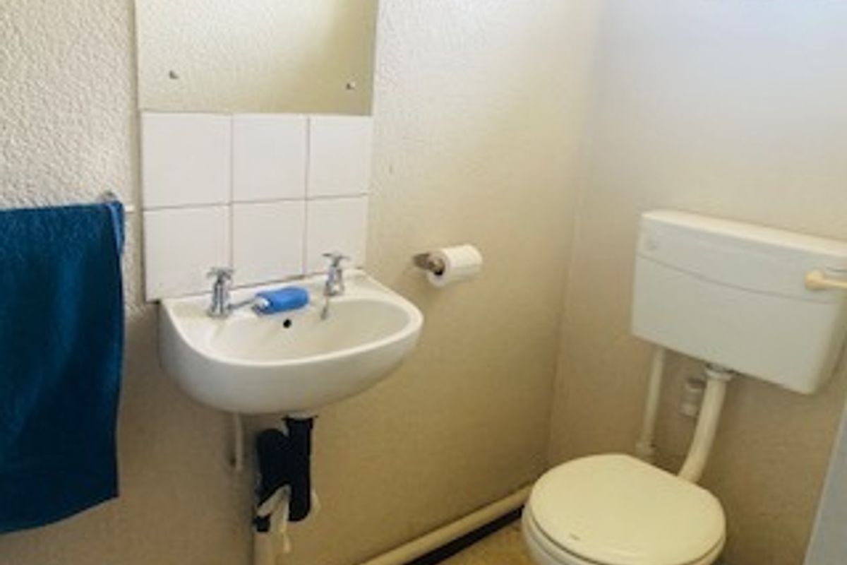 A compact bathroom featuring a wall-mounted basin with tiled splashback and a standard toilet, requiring cosmetic updates to improve the overall finish.