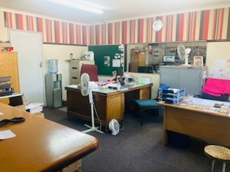 A functional office space featuring an internal service window and dated decorative wallpaper border, suitable for commercial administrative use.