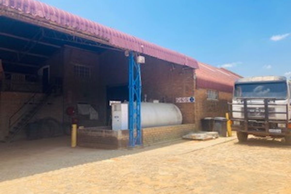 Commercial property exterior featuring a large brick warehouse structure with a corrugated metal roof and an on-site fuel storage tank.