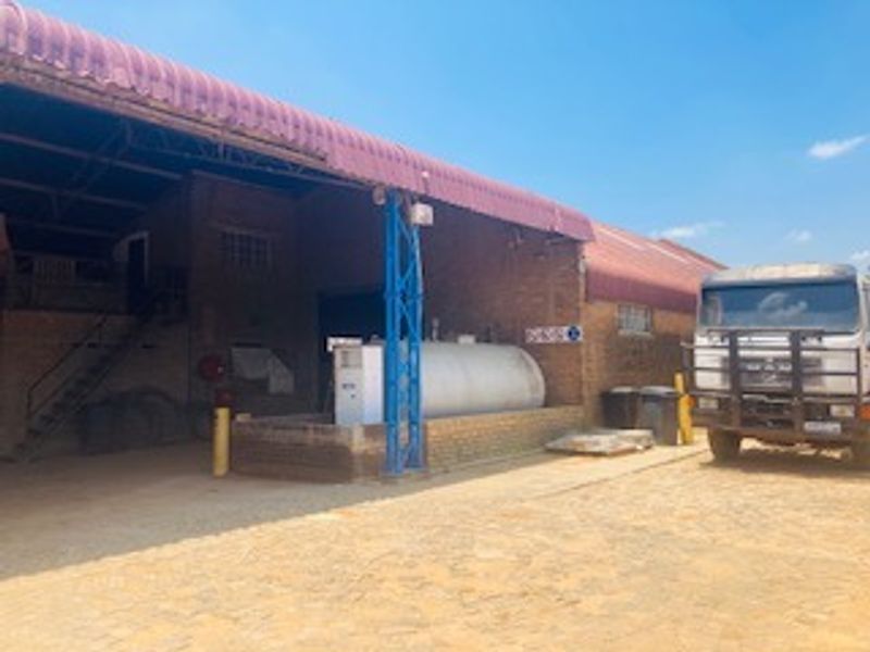 Commercial property exterior featuring a large brick warehouse structure with a corrugated metal roof and an on-site fuel storage tank.
