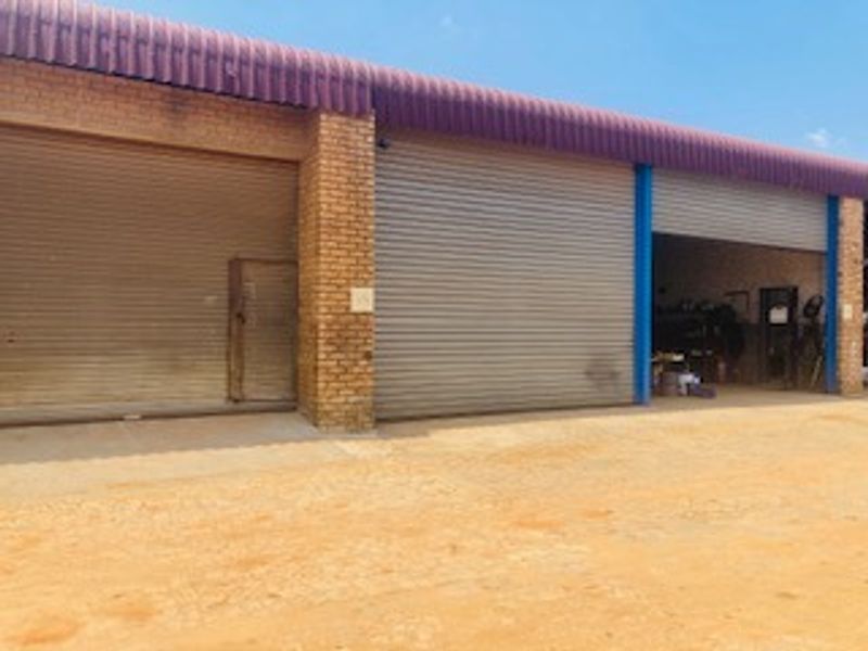 Commercial warehouse exterior featuring multiple roller shutter doors, brick facade, and a durable metal roof with a concrete apron.