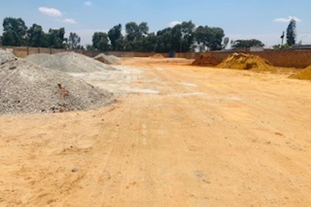 A view of a vacant commercial land plot featuring cleared ground and a perimeter boundary wall.