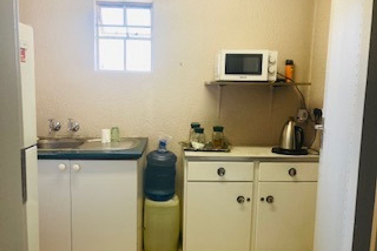 A compact kitchenette featuring basic built-in cabinetry, a stainless steel sink, and wall-mounted shelving, providing functional utility space.