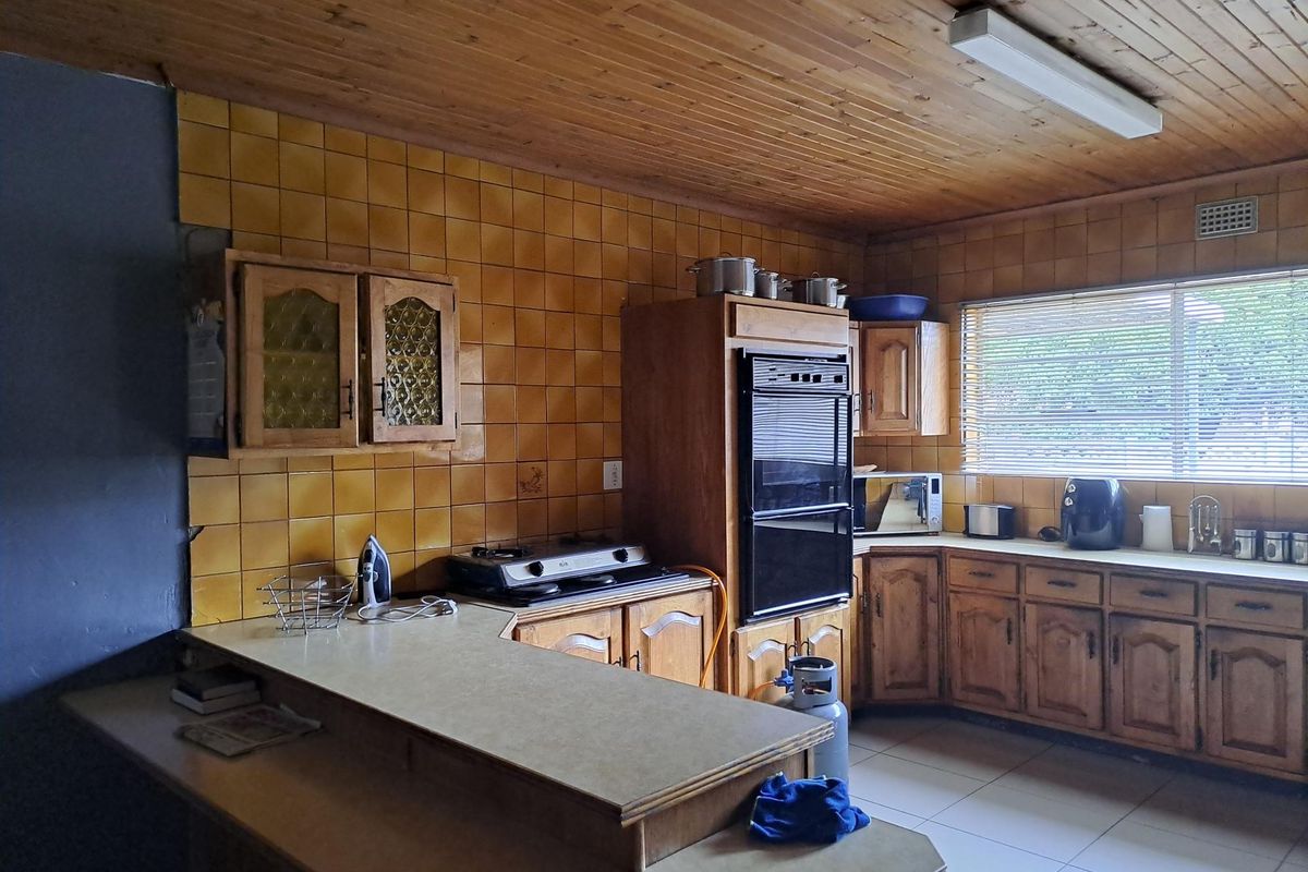 A dated kitchen featuring wooden cabinetry, a built-in oven, gas hob, and tiled splashbacks with a timber-paneled ceiling.