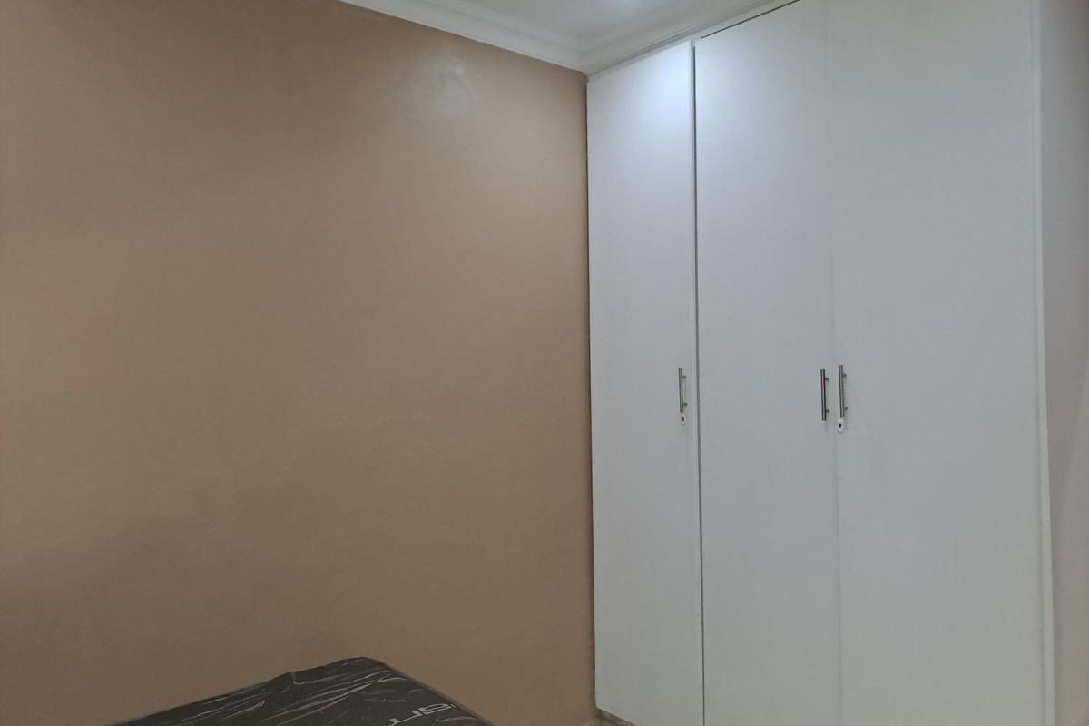A bedroom featuring neutral wall tones and white built-in cupboards with modern hardware, complemented by recessed ceiling lighting.