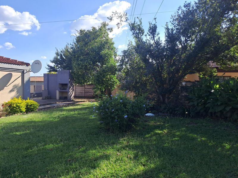 A spacious rear garden featuring a built-in braai area, established trees, and a well-maintained lawn enclosed by perimeter walls.