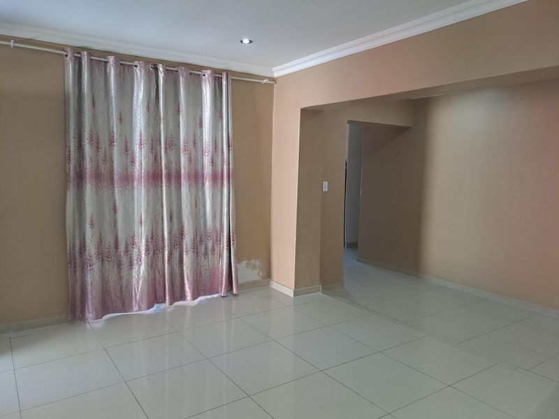 An empty living room featuring tiled flooring, recessed downlights, and coved cornicing, with some visible wall paint damage near the window area.