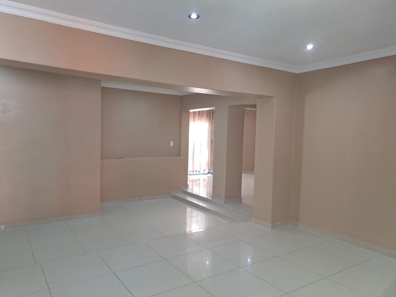An empty, open-plan living area featuring neutral-toned walls, tiled flooring, recessed downlights, and a built-in wall niche.