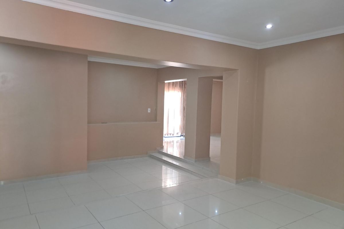 An empty, open-plan living area featuring neutral-toned walls, tiled flooring, recessed downlights, and a built-in wall niche.