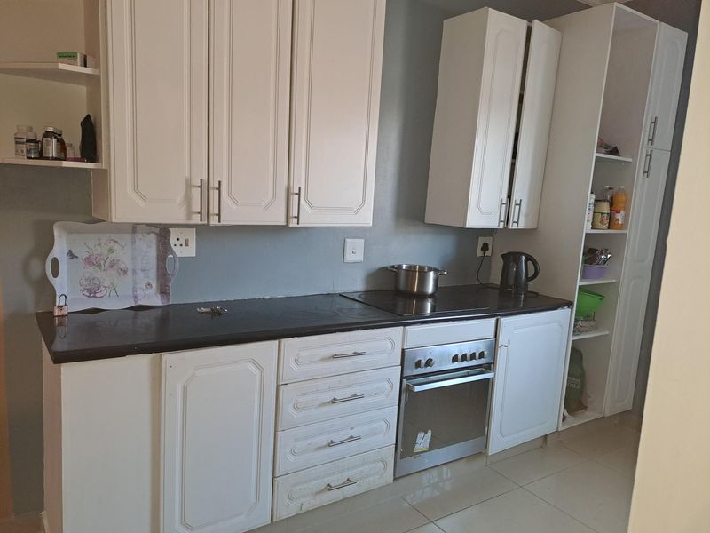 A functional kitchen featuring white cabinetry, dark countertops, a built-in oven, and an electric hob with tiled flooring.