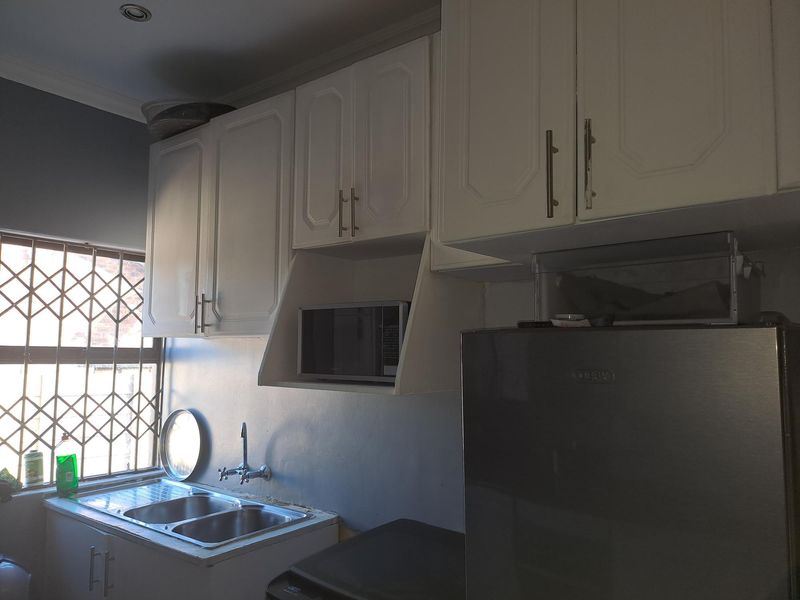 A functional kitchen featuring white built-in cabinetry, a double stainless steel sink, and a dedicated microwave shelf, with security bars on the window.