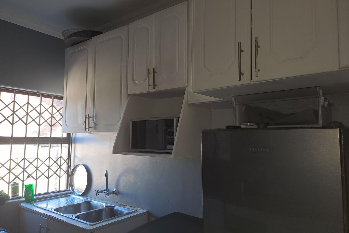 A functional kitchen featuring white built-in cabinetry, a double stainless steel sink, and a dedicated microwave shelf, with security bars on the window.