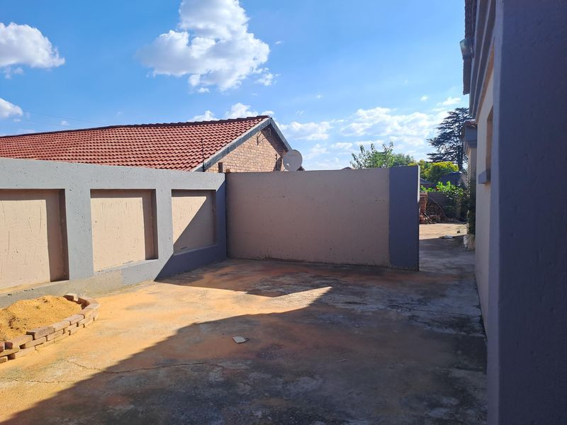 A rear exterior area featuring a concrete paved courtyard enclosed by boundary walls and a small brick planter.