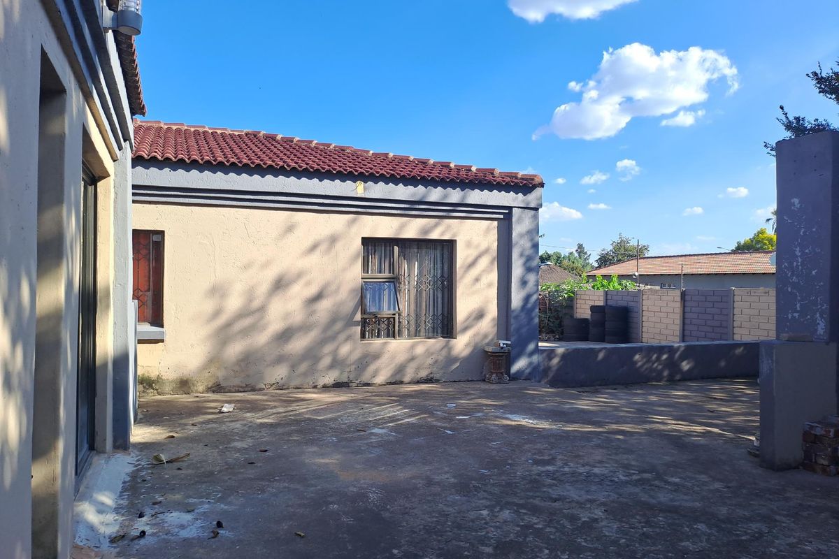 Rear exterior view of the property featuring a concrete patio area, tiled roof, and masonry boundary walling.