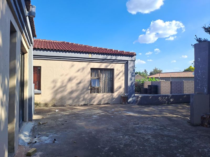 Rear exterior view of the property featuring a concrete patio area, tiled roof, and masonry boundary walling.