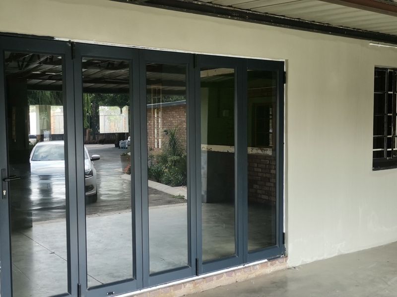 A covered patio area featuring modern dark aluminium stacker doors, concrete flooring, and exposed brick accents, providing a functional outdoor transition space.