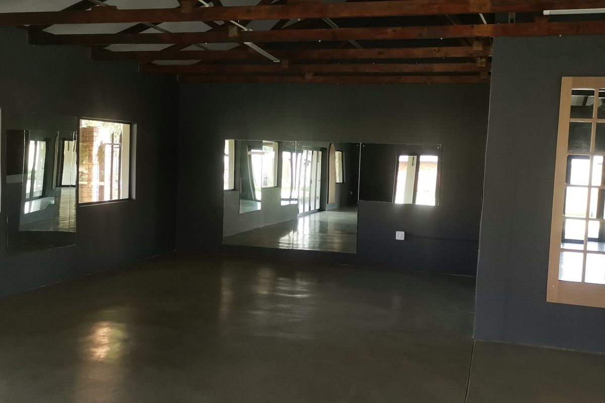 Spacious studio or gym area featuring polished concrete floors, exposed timber roof trusses, and large wall-mounted mirrors, offering a versatile open-plan layout.