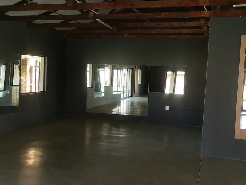 Spacious studio or gym area featuring polished concrete floors, exposed timber roof trusses, and large wall-mounted mirrors, offering a versatile open-plan layout.