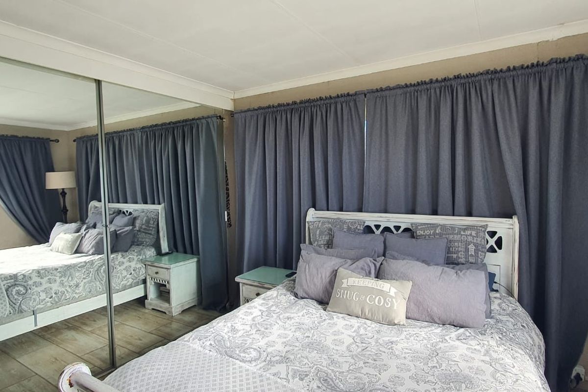 A bedroom featuring large mirrored sliding wardrobe doors and a glass block window, providing natural light and a sense of space.