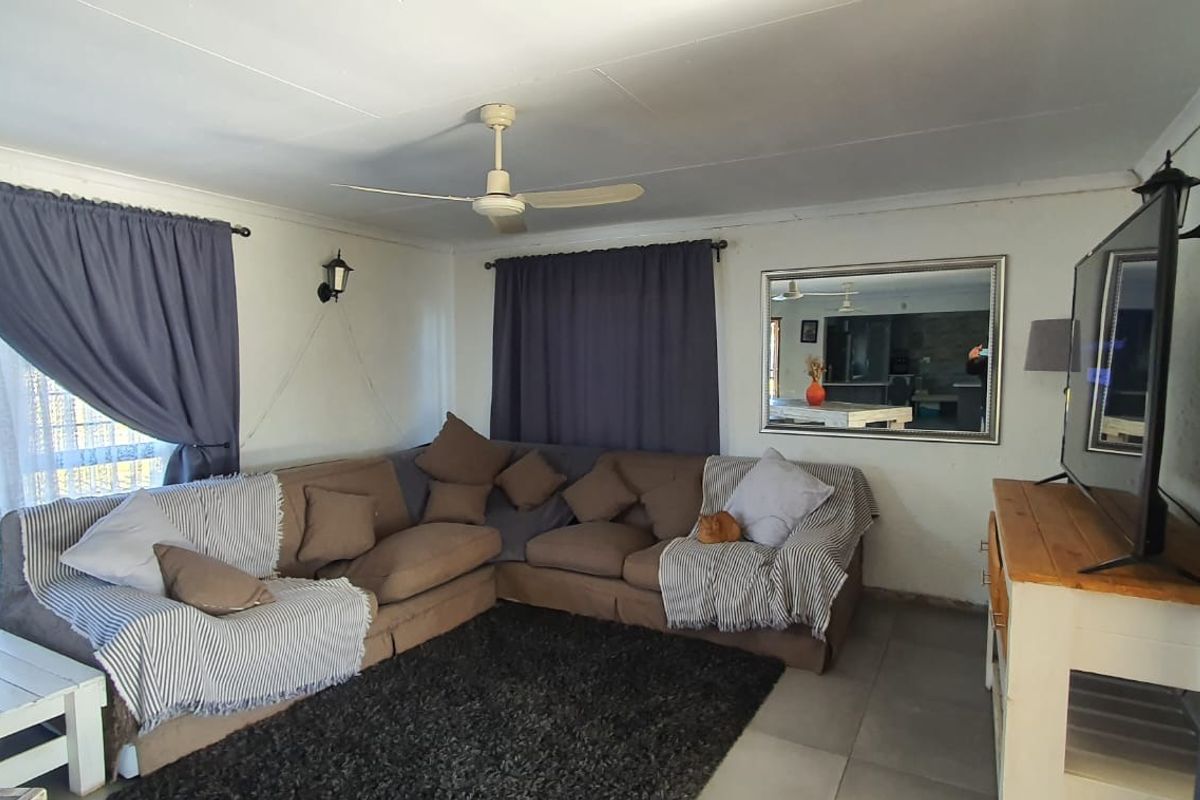 A comfortable living room featuring tiled flooring, a ceiling fan, and wall-mounted lighting fixtures.