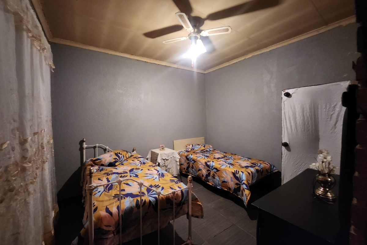 A bedroom featuring tiled flooring, a ceiling fan, and neutral wall tones, providing a functional sleeping space.