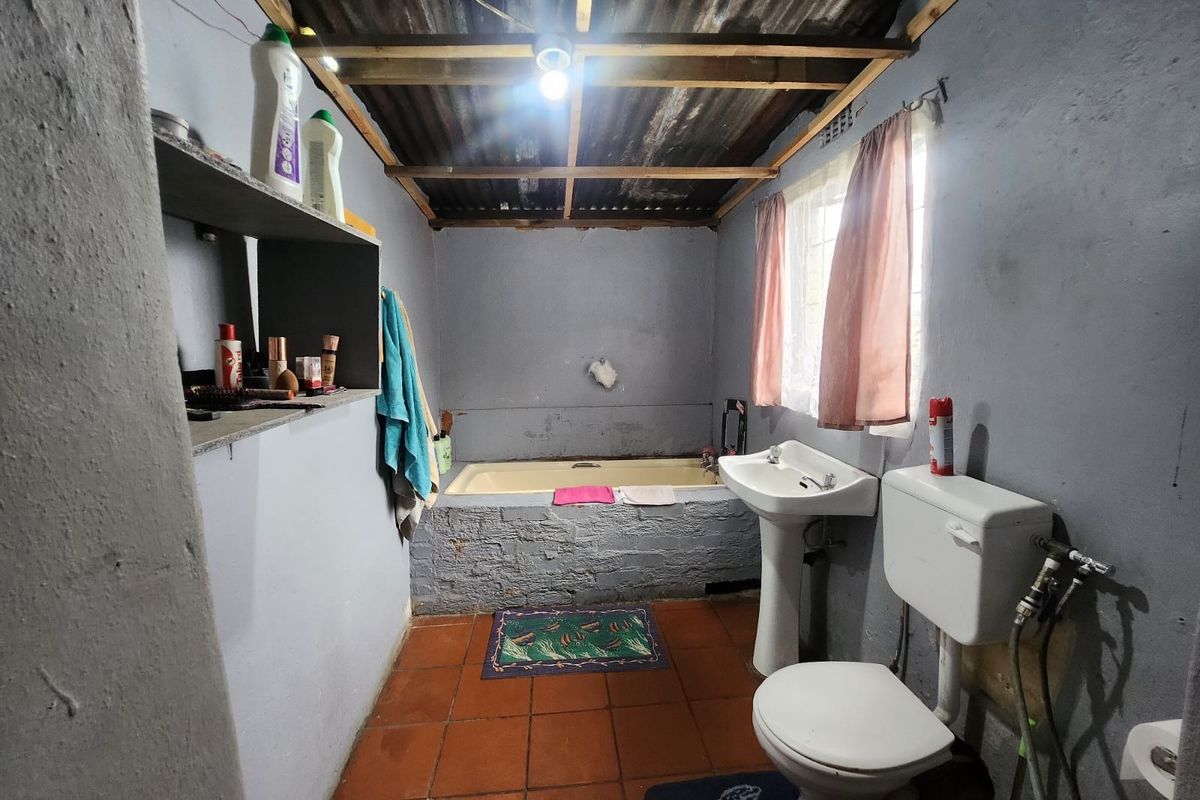 A basic bathroom featuring a pedestal basin, toilet, and a built-in bathtub with an exposed corrugated iron roof structure.