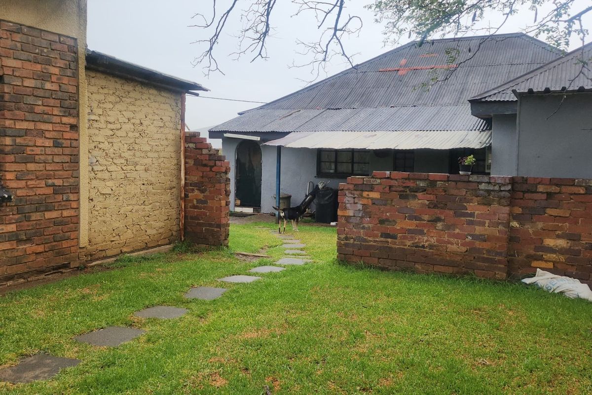 Rear view of the property showing a garden area, brick boundary walls, and the main dwelling structure with a corrugated metal roof.