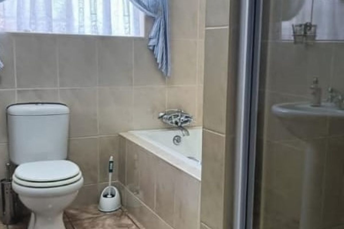 A functional bathroom featuring a tiled bathtub, pedestal sink, and a separate shower enclosure with neutral wall tiling.