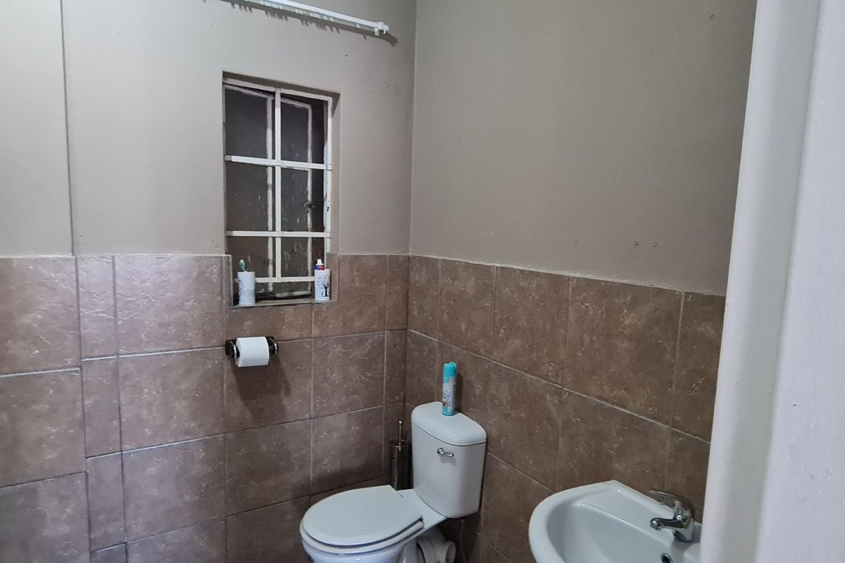 A functional bathroom featuring tiled walls, a standard toilet, and a wall-mounted basin with a small window.
