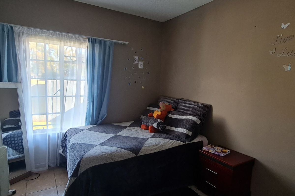 A bedroom featuring tiled flooring and a window with curtain tracks, providing natural light to the space.
